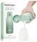 'A hand pours milk from a green Momcozy portable water and milk warmer into a bottle, with the product box beside it.'