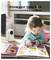 A toddler looks at a colorful book while a baby monitor camera appears nearby. Text above reads 'Know your baby is ok anytime anywhere in the house.'