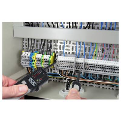 Technician testing an electrical control panel with a digital meter while holding probes near wiring and terminal blocks.
