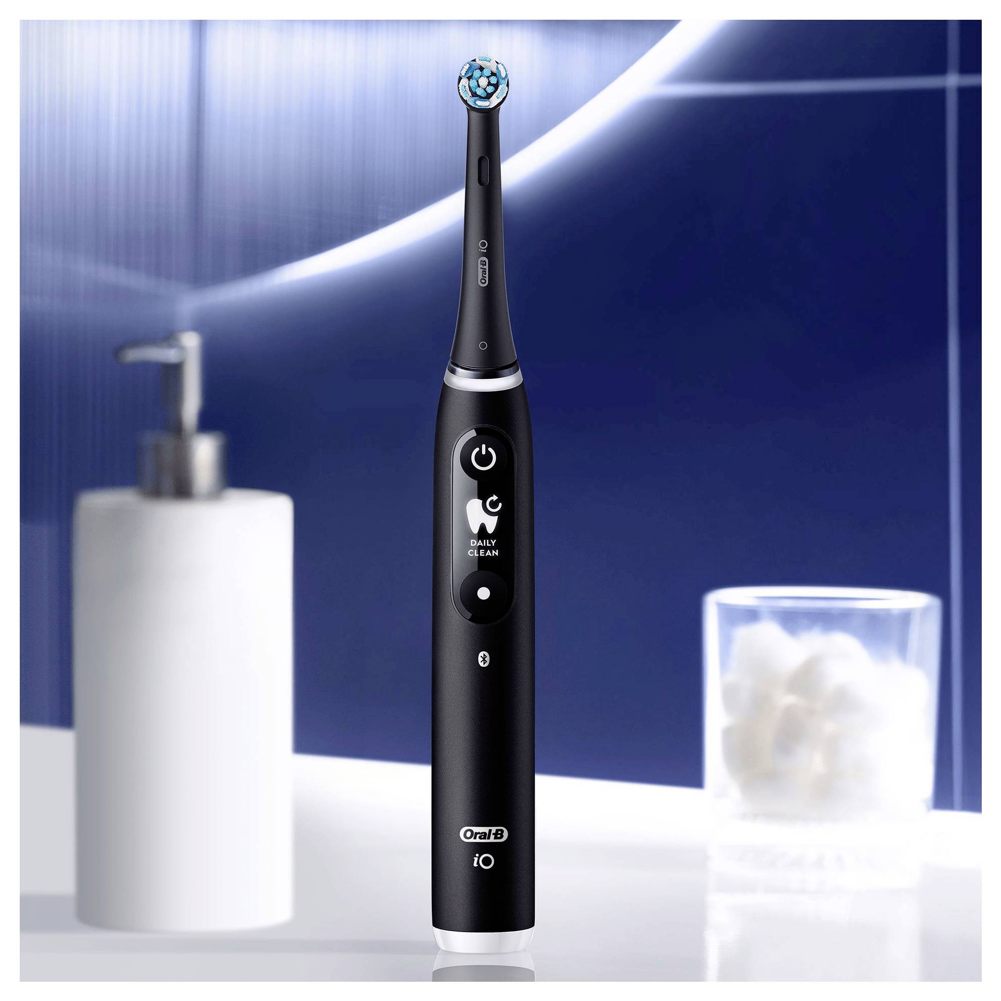 A black electric toothbrush stands upright on a bathroom counter. A lotion dispenser and a glass container with cotton balls are in the background.