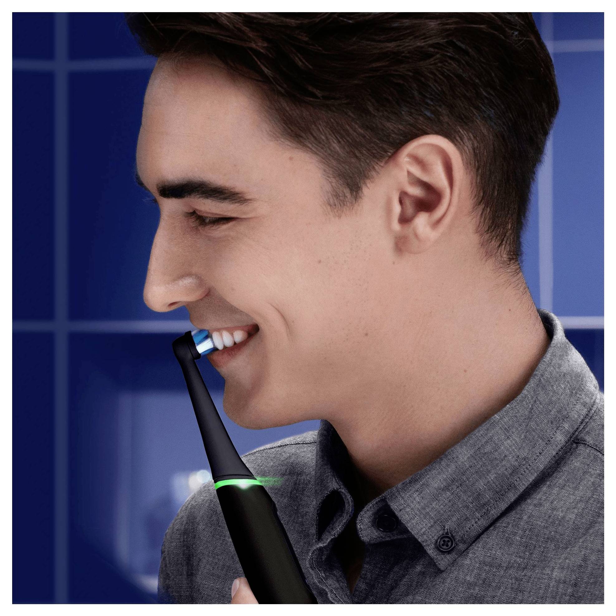 A person is using an electric toothbrush while smiling, set against a blue background with a tiled texture.