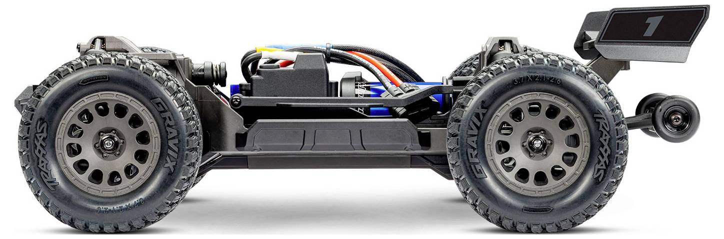 Side view of a remote-controlled off-road vehicle with large tires, exposed wiring, and a rear spoiler. Appears built for rugged terrain.