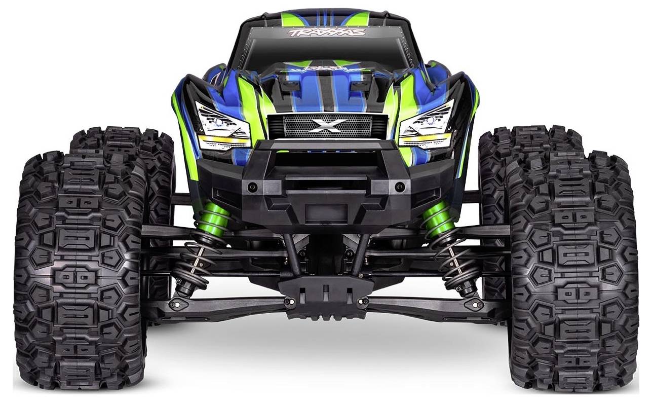 A blue and green toy monster truck with large, textured tires and suspension springs is shown from the front, emphasizing its robust design.