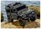 A small black off-road toy vehicle resembling a Defender model is parked on rough rocks near a body of water, showcasing its rugged design.