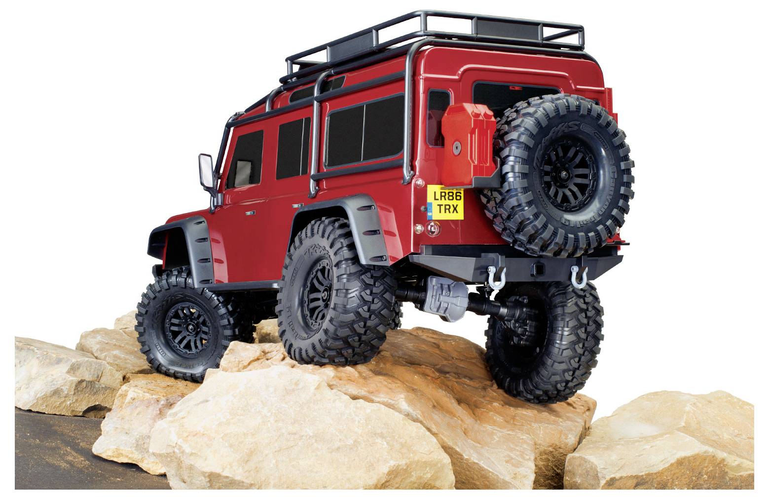 A red off-road RC vehicle climbs over large rocks, showcasing its rugged design and large tires. The focus highlights its off-road capability.