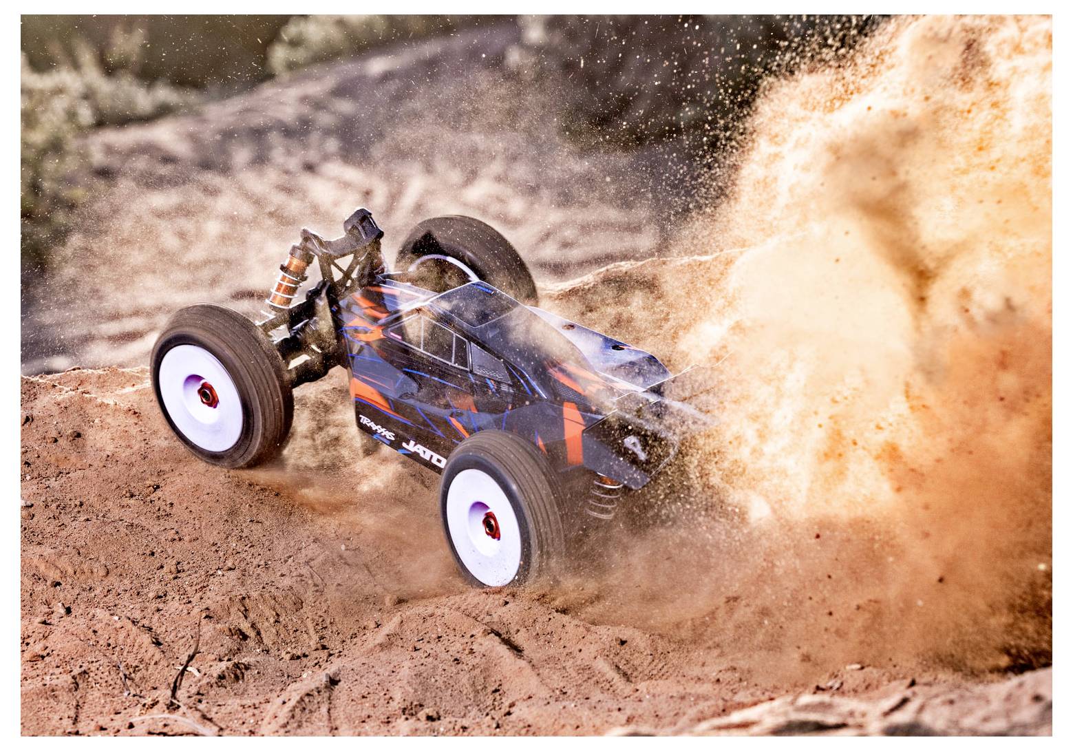 A remote-controlled car with blue and orange stripes kicks up a large cloud of dust as it races up a sandy hill.