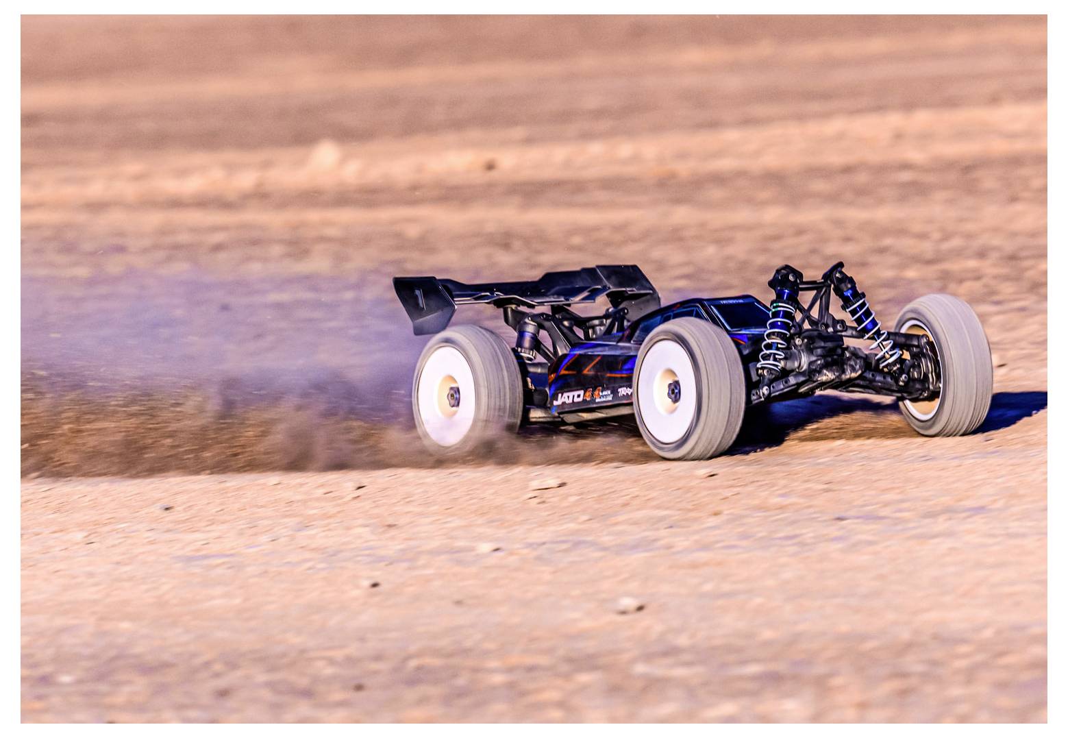 'A remote-controlled car speeds across a sandy landscape, kicking up dust as it moves. The sun casts shadows, highlighting the car's details.'