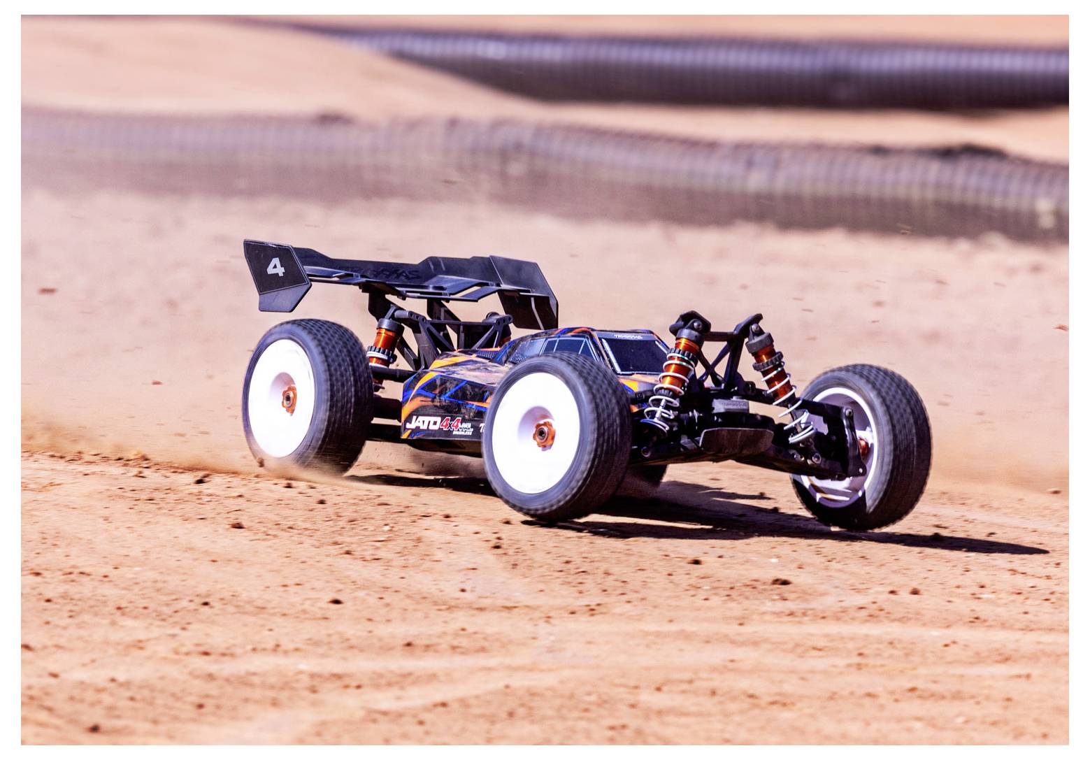 A remote-controlled car speeds across a dusty track, kicking up dirt, under a clear sky.