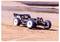 A remote-controlled car speeds across a dusty track, kicking up dirt, under a clear sky.