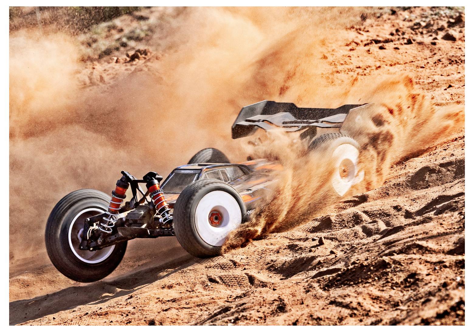A remote-controlled car speeds through sandy terrain, kicking up dust as it navigates a turn on a sunny day.