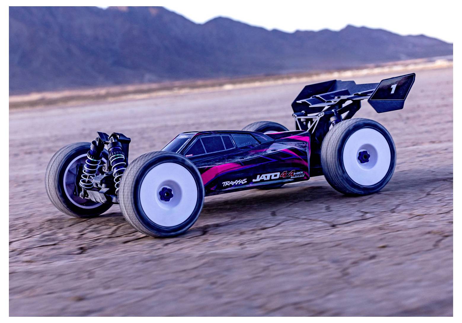 A remote-controlled car with large wheels speeds across a barren desert landscape, with mountains in the background.