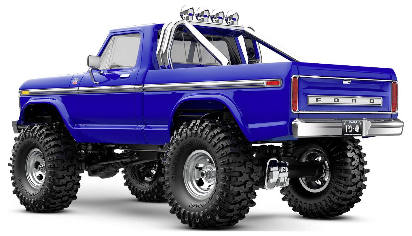 A bright blue lifted pickup truck with large off-road tires and a rear roll bar, viewed from the back angle.