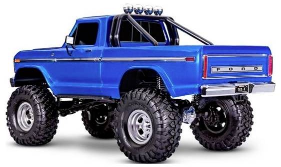 A blue lifted pickup truck with large off-road tires, a roll cage, and a 'FORD' logo on the back, viewed from the rear side.