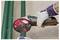 A person wearing protective gloves uses an electric grinder to cut green metal pipes, with sparks flying during the cutting process.