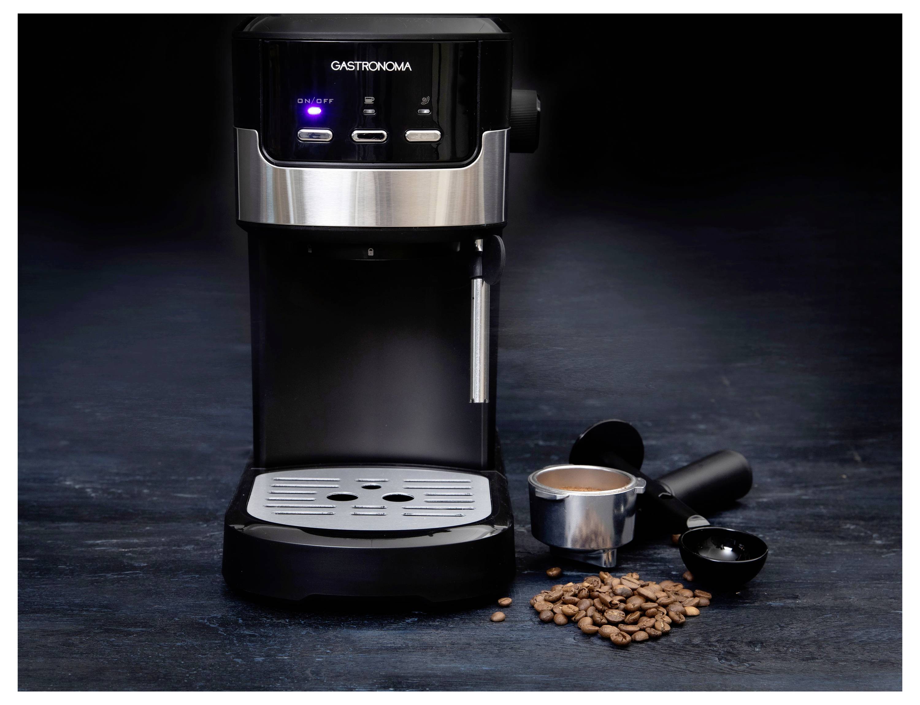 Espresso machine on a dark surface with a filter holder, ground coffee, and beans nearby, suggesting coffee preparation.