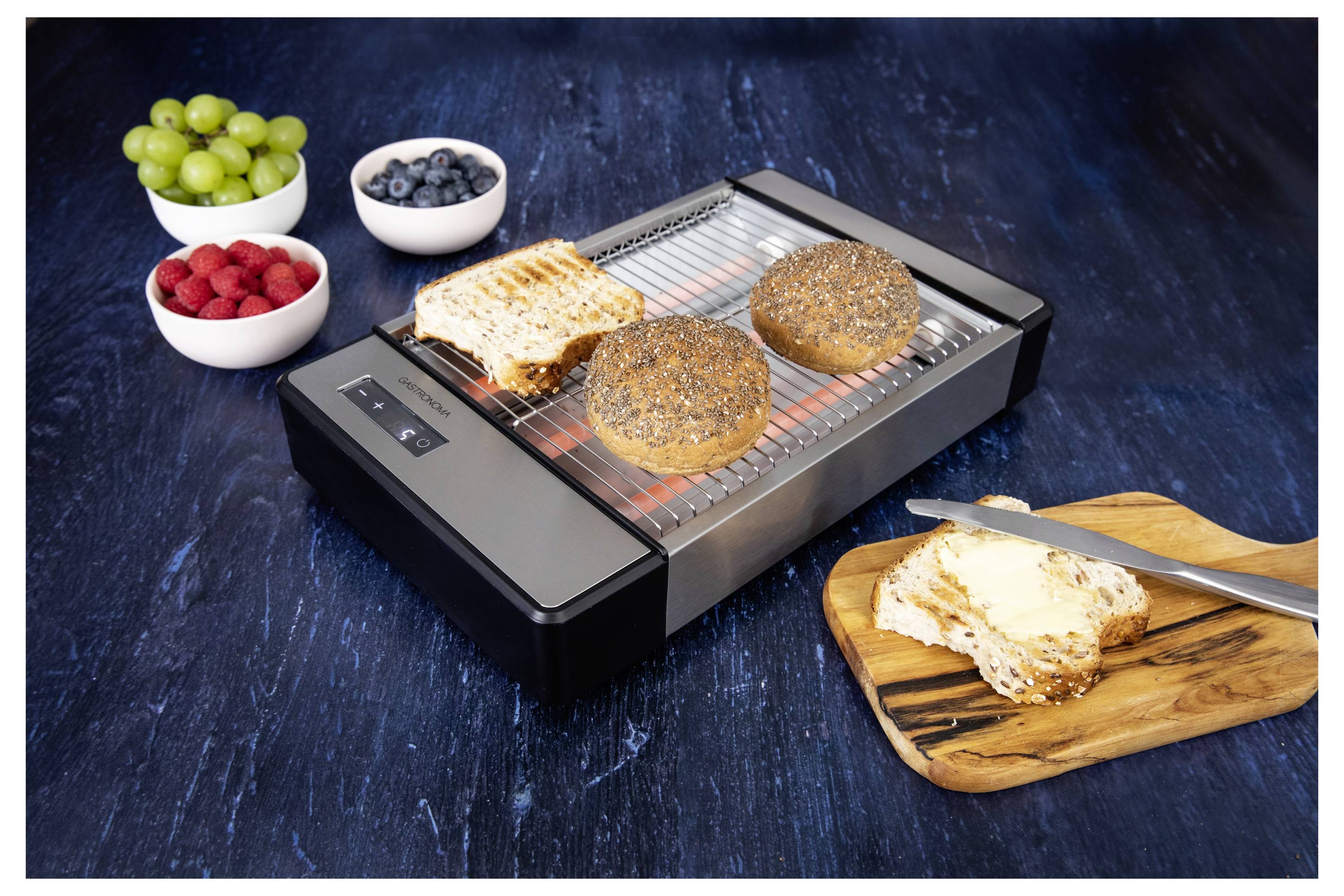 'Toaster grilling bread and a bagel, knife on a buttered slice, with bowls of grapes, blueberries, and raspberries on a dark surface.'