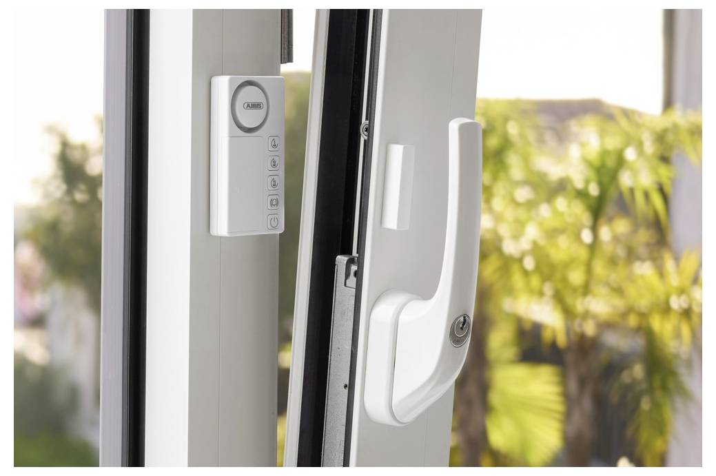 'A partially open sliding glass door with a white handle and a wall-mounted control panel with buttons nearby; blurred greenery outside.'