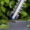 A hedge trimmer resting on a concrete surface is surrounded by lush green leaves, indicating gardening or landscaping activity.