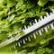 A hedge trimmer cutting through dense green leaves, highlighting garden maintenance and tool effectiveness.