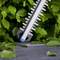 A hedge trimmer blade with sharp teeth, positioned among green leaves, suggesting it's designed for cutting or shaping hedges.