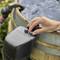 A person adjusts knobs on a water control device next to a rain barrel, indicating water flow or pressure settings.