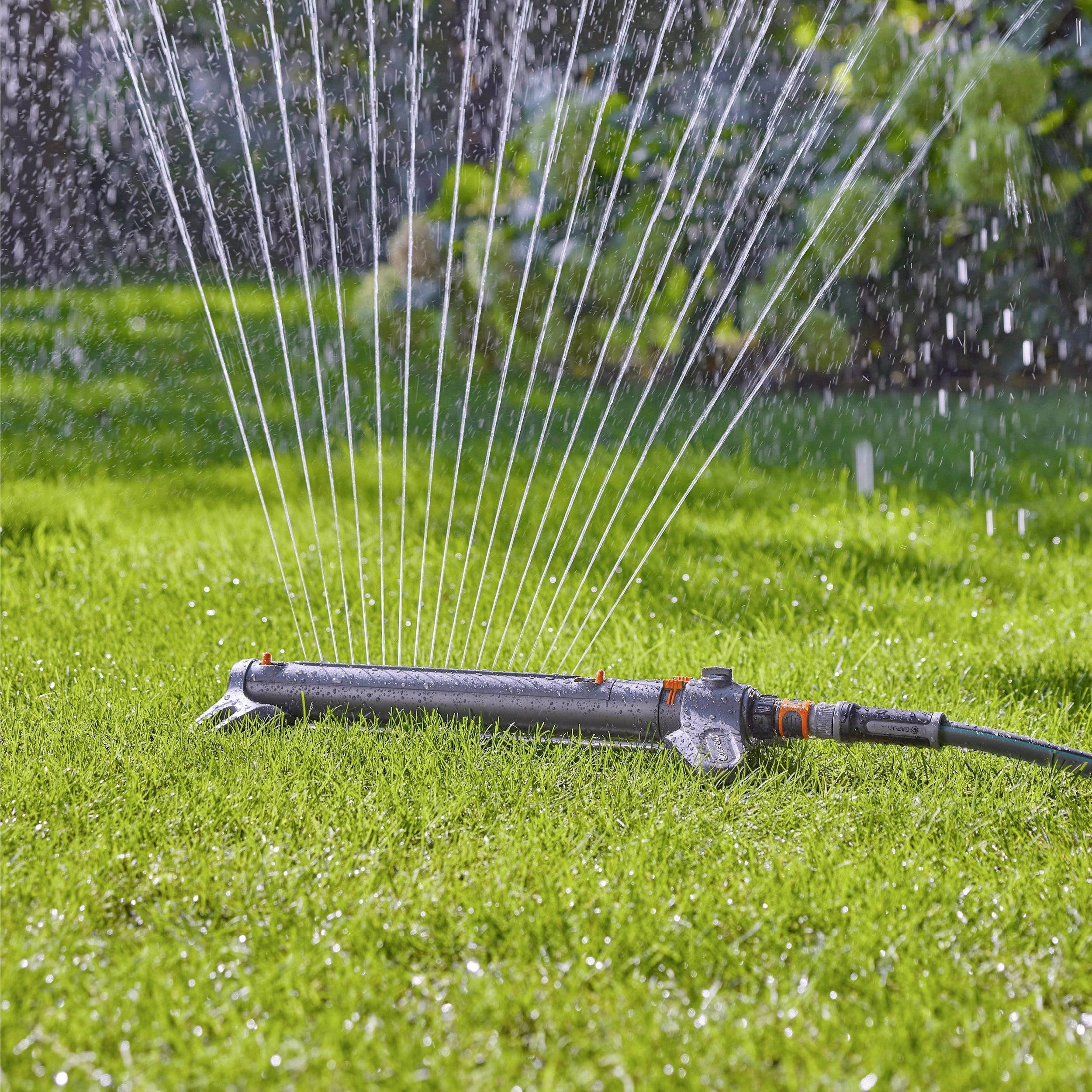A sprinkler waters a lush, green lawn, spraying water in a wide arc under bright sunlight.