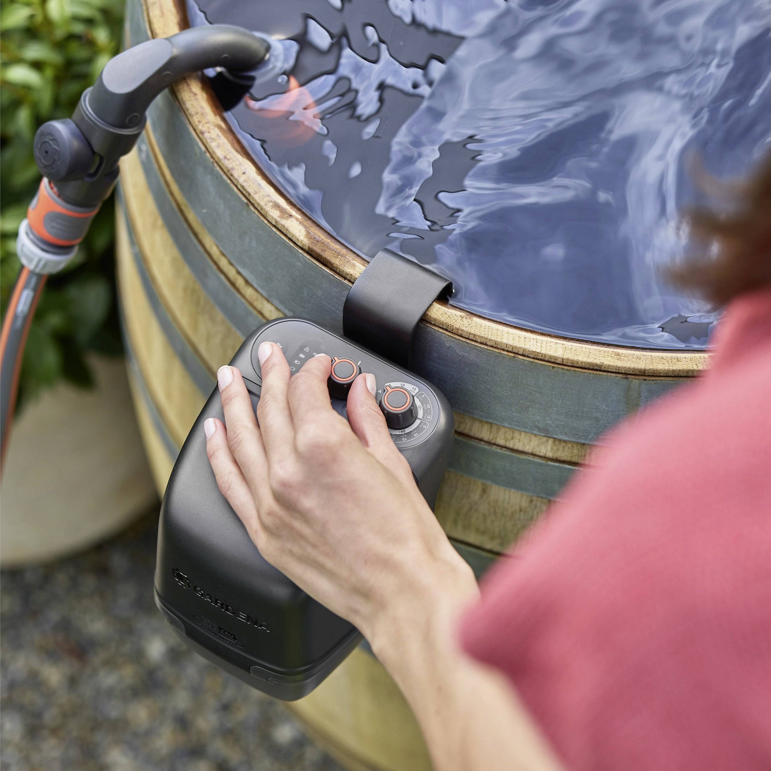 A person adjusts the settings on a black control panel attached to a wooden hot tub, with water gently rippling inside.