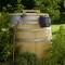 A wooden rain barrel with a hose attached is placed in a garden surrounded by greenery, used for collecting rainwater.