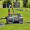 A portable garden pump on grass with sprinklers in the background. The pump is branded 'Gardena 5000/5E'.
