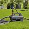 A garden pump sits on green grass with hoses attached, actively watering the lawn and nearby plants.