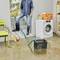 A person in boots stands in a flooded laundry room with a washing machine, chair, broom, and basket partially submerged in water.