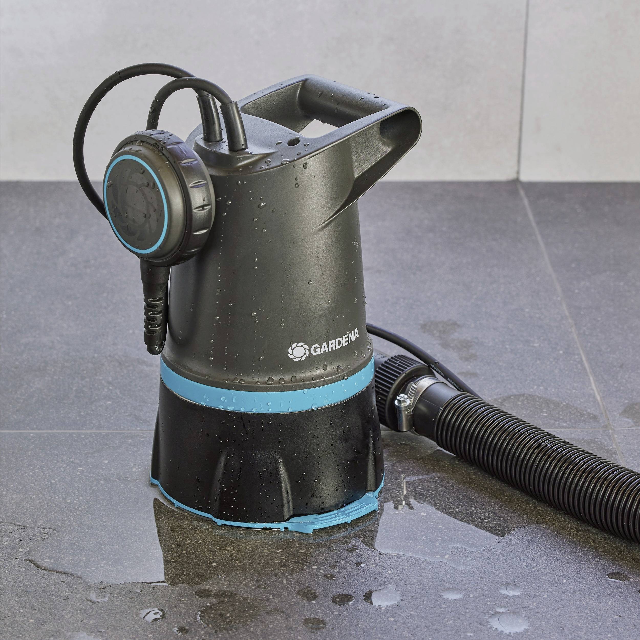 A black and blue water pump with a hose attached, placed on a wet stone floor. The brand name 'Gardena' is visible on the pump.