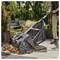 A person uses a garden leaf collector on a patio, gathering fallen leaves. The tool is wheeled, with a mesh bag for leaf collection.