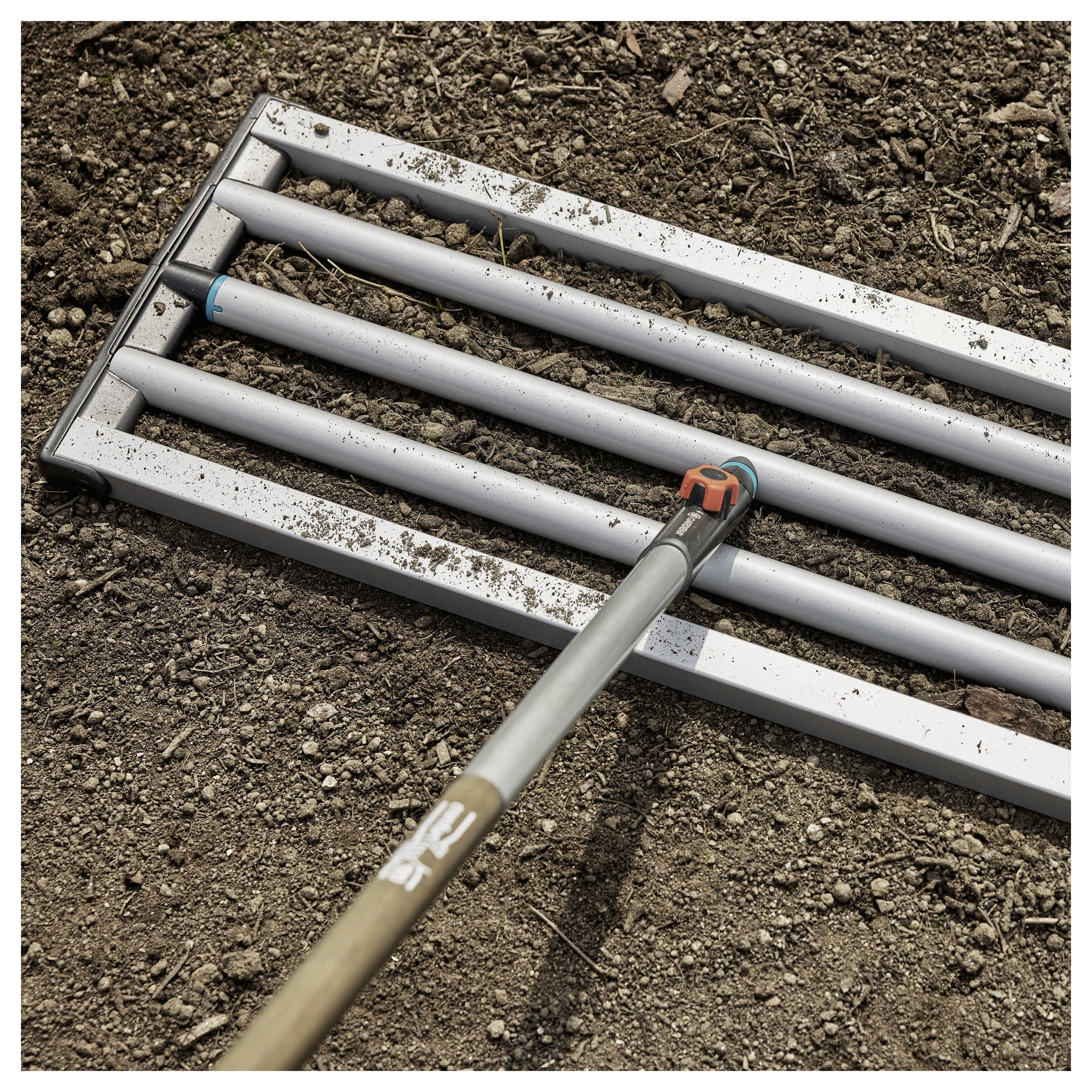 A metal rake with a wooden handle lies on freshly tilled soil, suggesting garden preparation or landscaping activities.