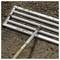 A metal rake with a wooden handle lies on freshly tilled soil, suggesting garden preparation or landscaping activities.