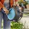 A person in a garden holding a retractable garden hose reel, with one hand on the handle and the other adjusting the hose.