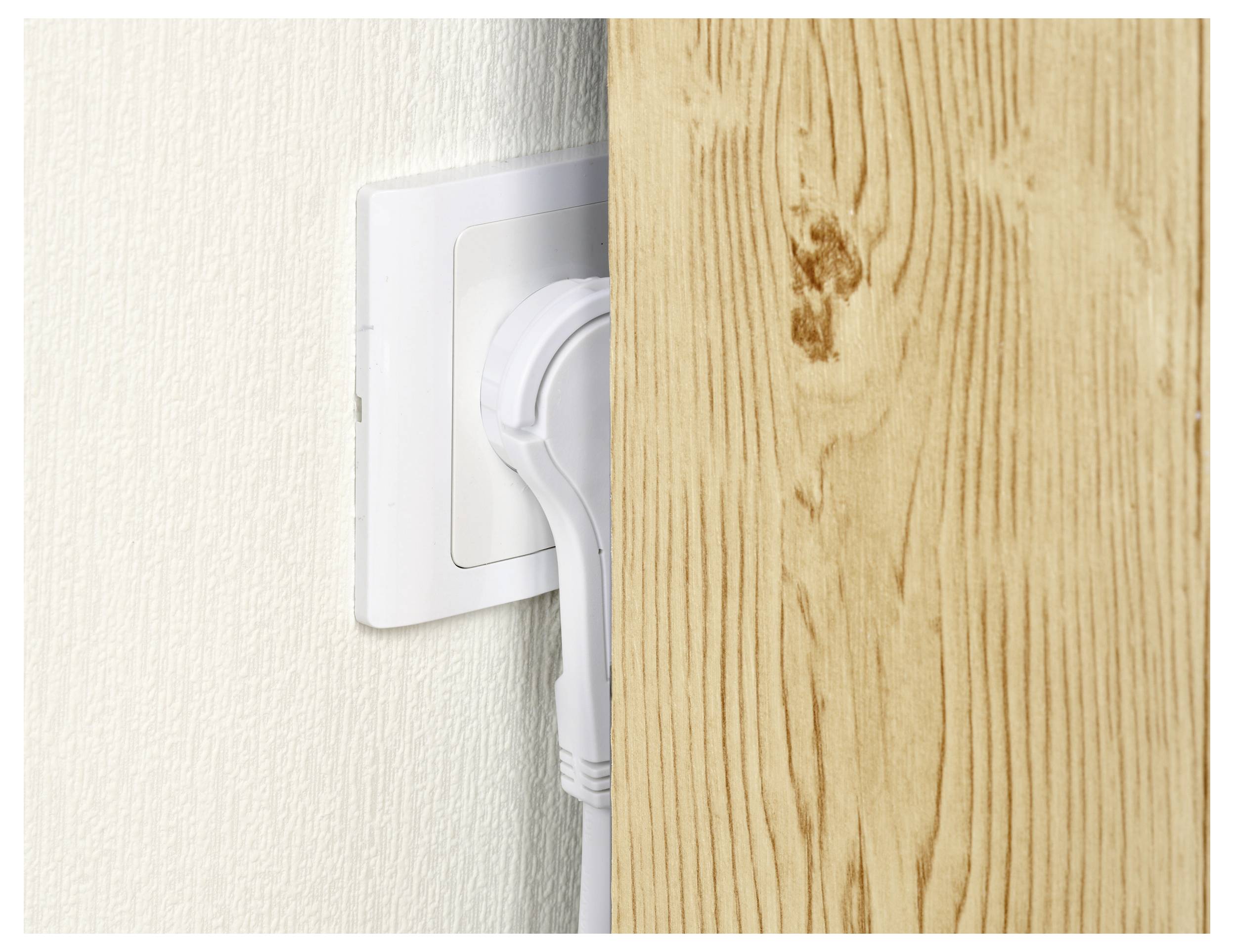 A wooden board dangerously positioned close to an electrical socket, partially covering a plug.