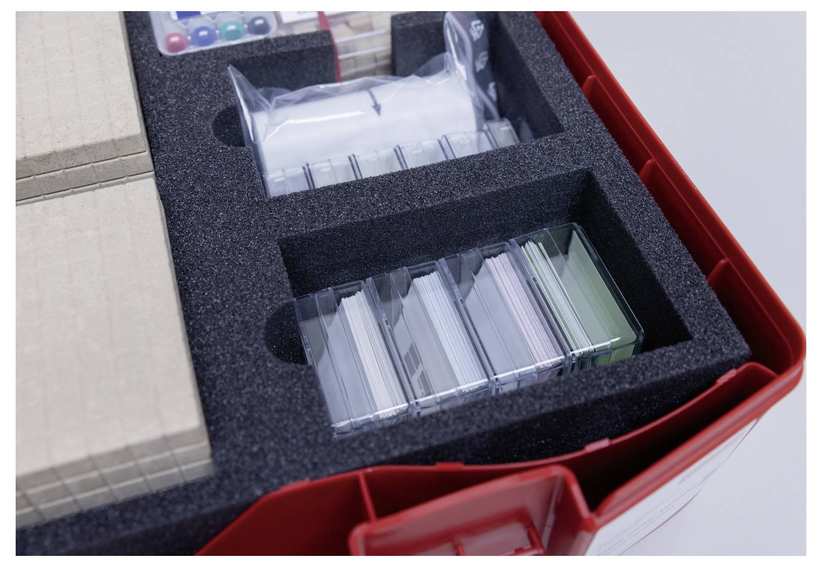 'Laboratory kit containing slides, vials, and cardboard pieces arranged in a foam holder within a red plastic case.'