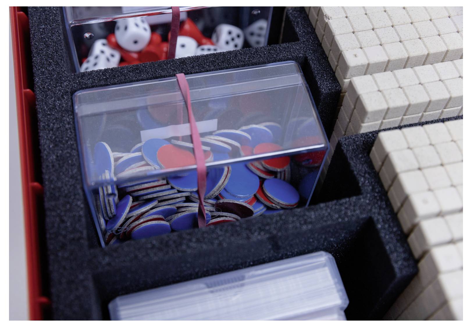 'A game box containing blue and red chips, dice, and wooden blocks organized in sections.'