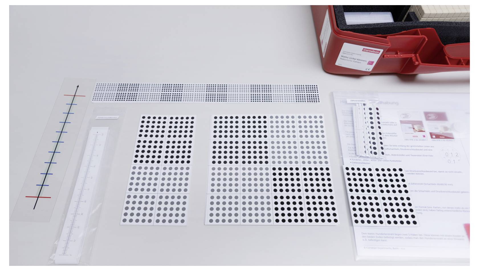 Assortment of calibration tools and dot pattern sheets on a table next to a red case, likely used for testing or alignment purposes.