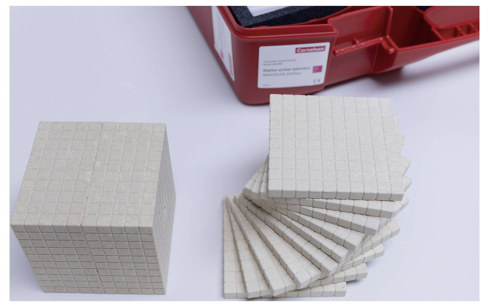 'A red box containing mathematical counting blocks, including a cube and several flat squares, used for teaching arithmetic basics.'