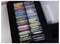 A box containing neatly arranged colored slide holders with white labels, used for storing microscope slides, organized in rows on foam.