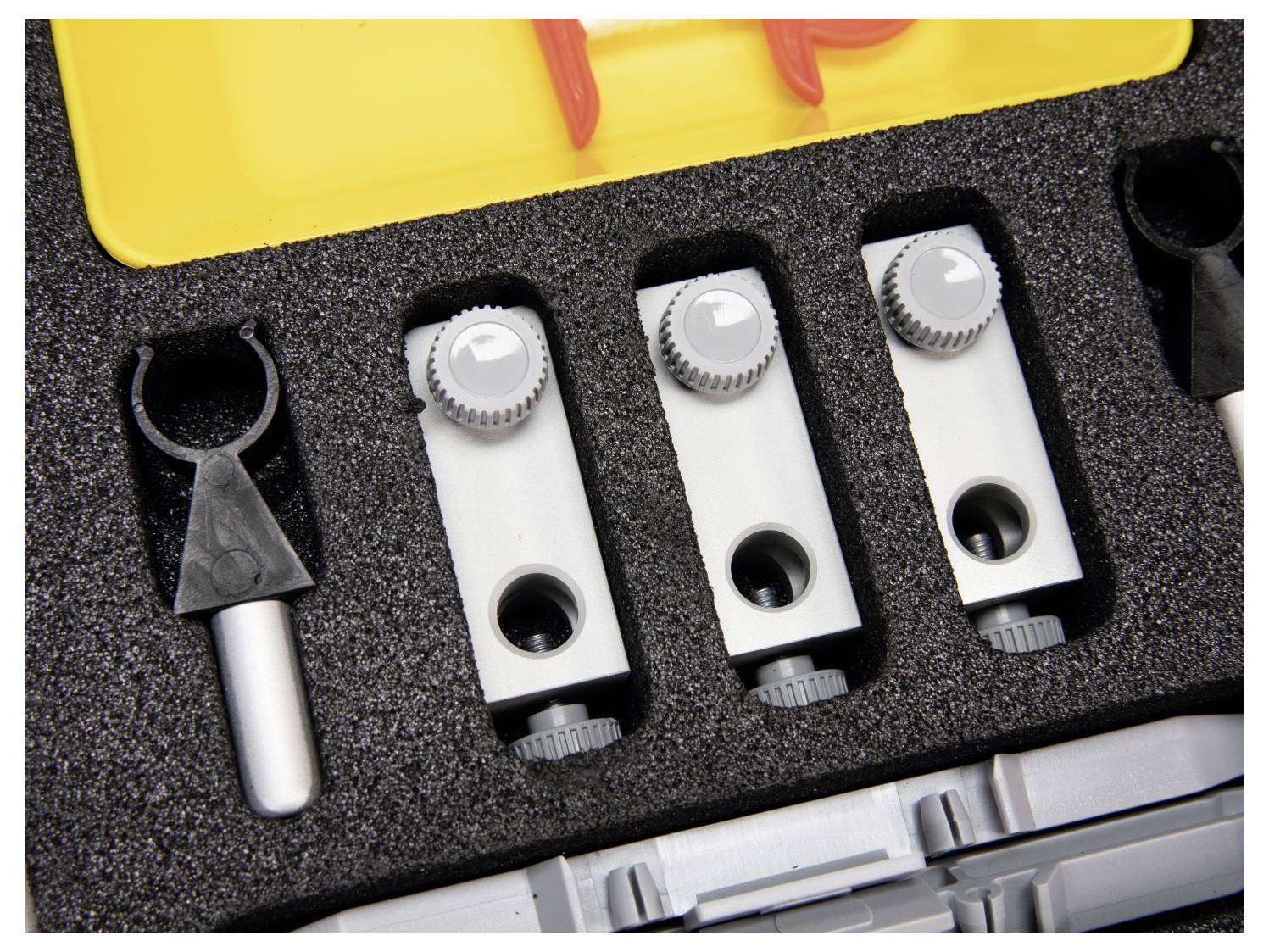 Storage case with custom foam insert holding three grey tools with dials and a black handle on the left. Yellow and red elements on top.