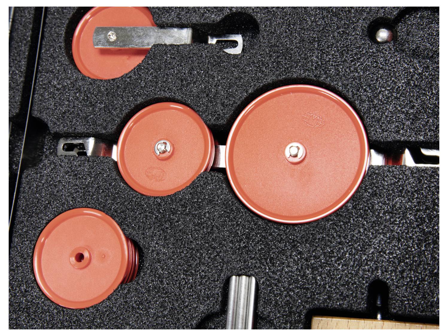 The image shows a set of red circular disk tools of various sizes arranged in a black foam case.