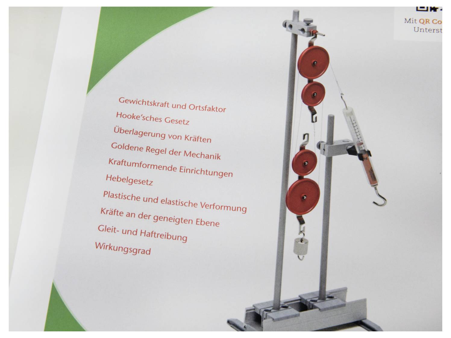 'Physics equipment showcasing pulley system with red weights and measurement tool, alongside a list of German physics concepts.'