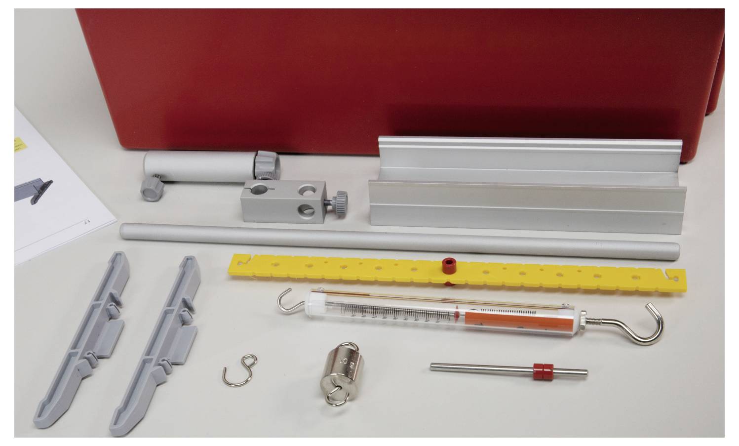 'Parts of an assembly kit displayed on a table, including metal rods, connectors, a syringe-like tool, and other components, against a red backdrop.'
