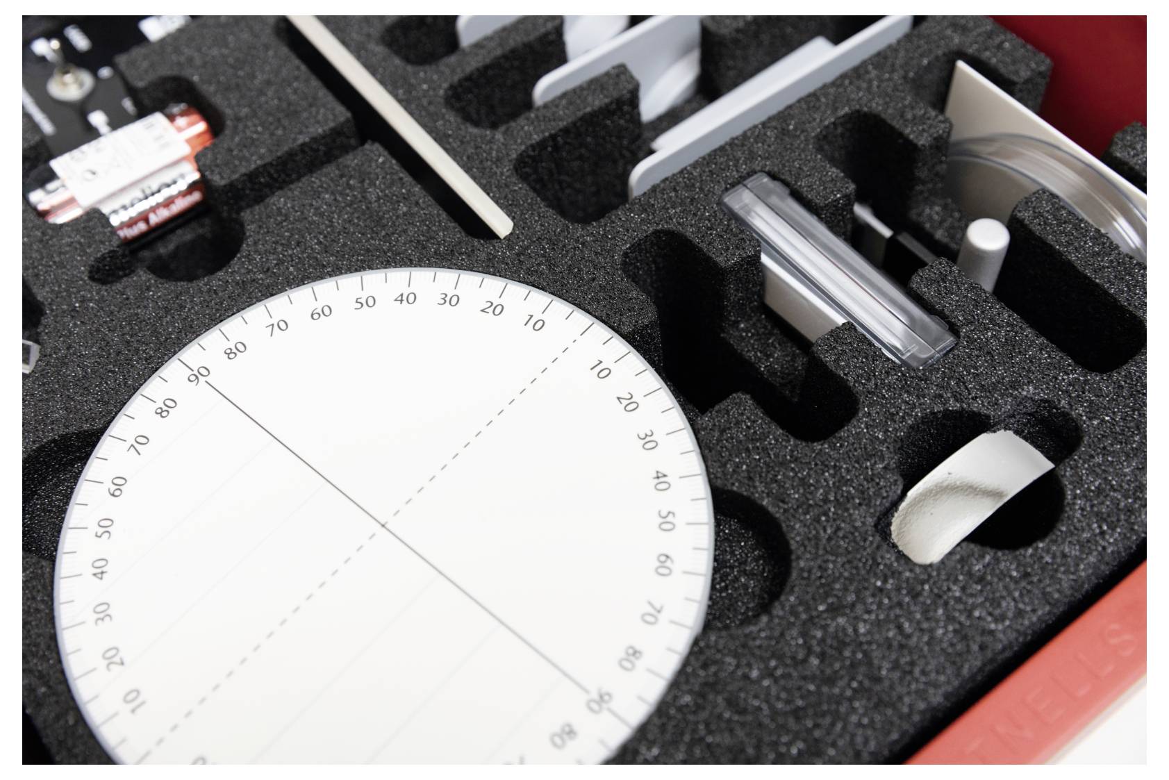 A red case with foam compartments holds various precision instruments, including a circular protractor marked in degrees.