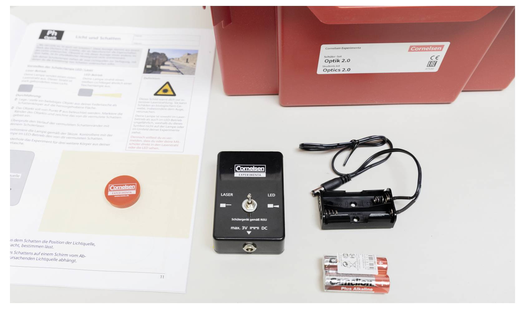 An educational kit with a manual, laser device, battery holder, batteries, and red box labeled 'Cornelsen' for physics experiments.