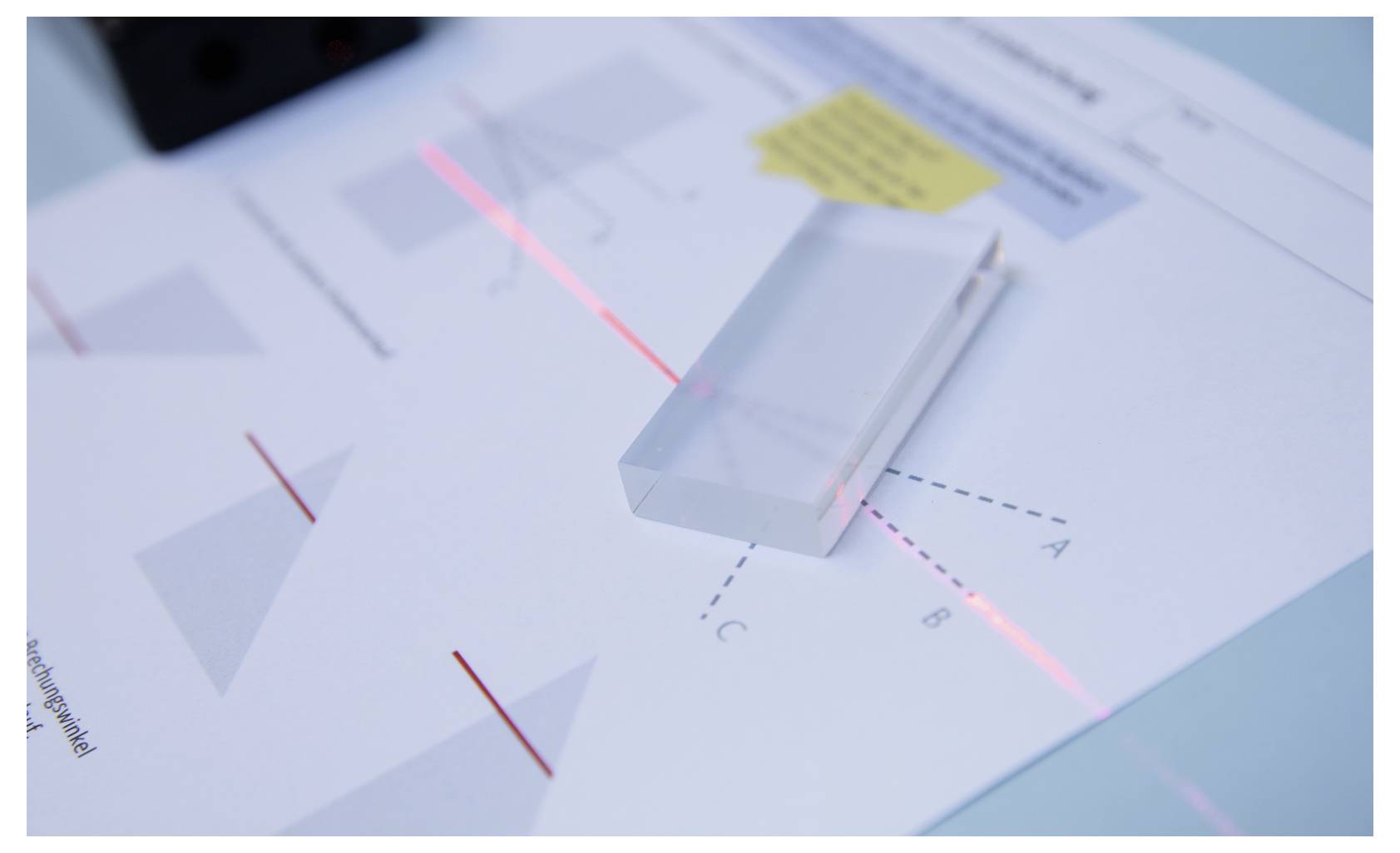 'A beam of light passes through a transparent prism, refracting into different paths marked A, B, and C on a worksheet underneath.'