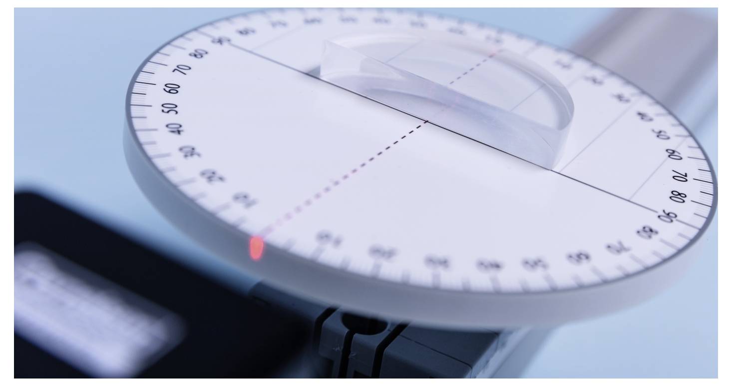 A close-up of a protractor with a semi-circular scale, showing measurements. A red laser points at a specific degree mark.